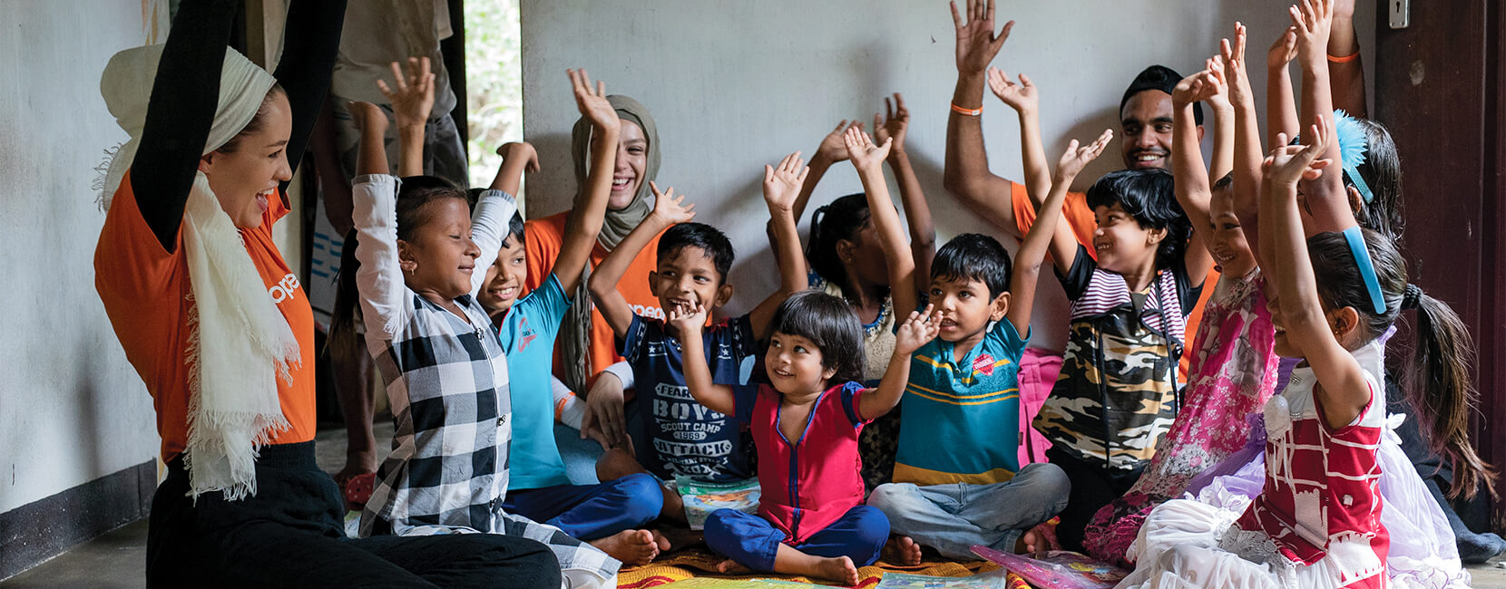 A group of smiling children wave their hands in the air